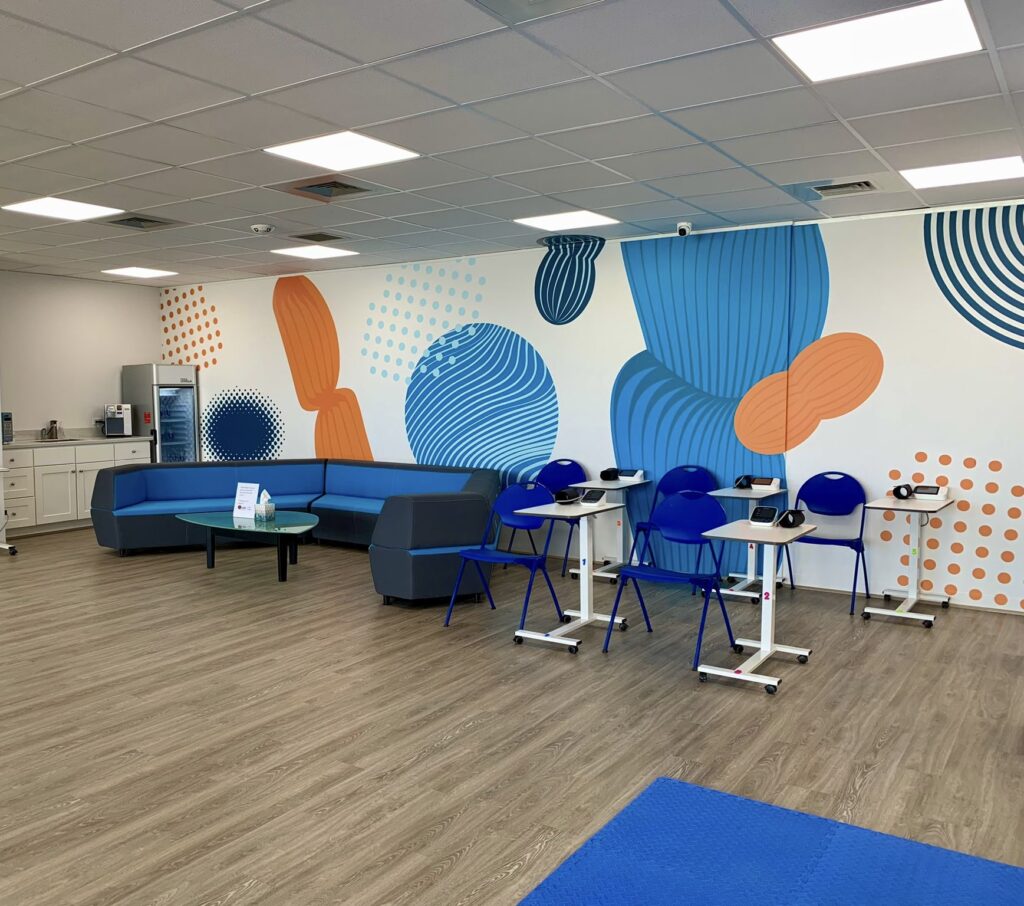 Modern lounge with a blue sectional sofa, small tables, and chairs. Vibrant abstract wall art in blue and orange tones. Cozy and inviting atmosphere.
